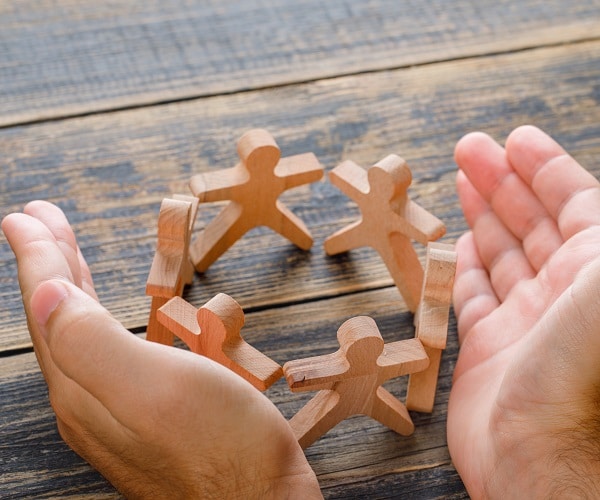 Business success concept on wooden background high angle view. hands protecting wooden figures of people.